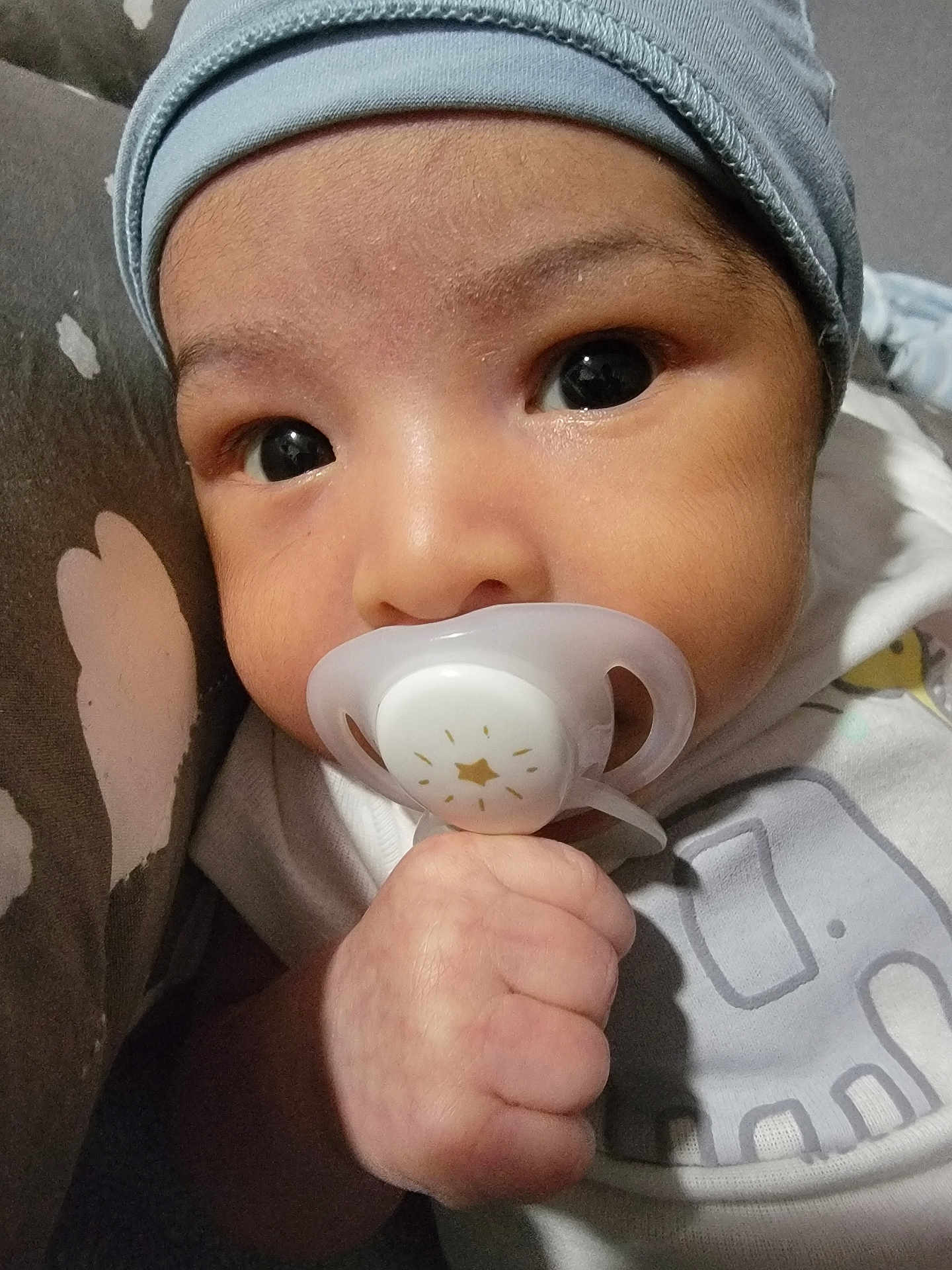 Eythan is registered to the contest to win money with this photo: baby, pacifier, hand, face, clothing, hat, infant, closeup, cute, child, skin, portrait, young, indoors, cozy, expression, newborn, sleepwear, holding, curious