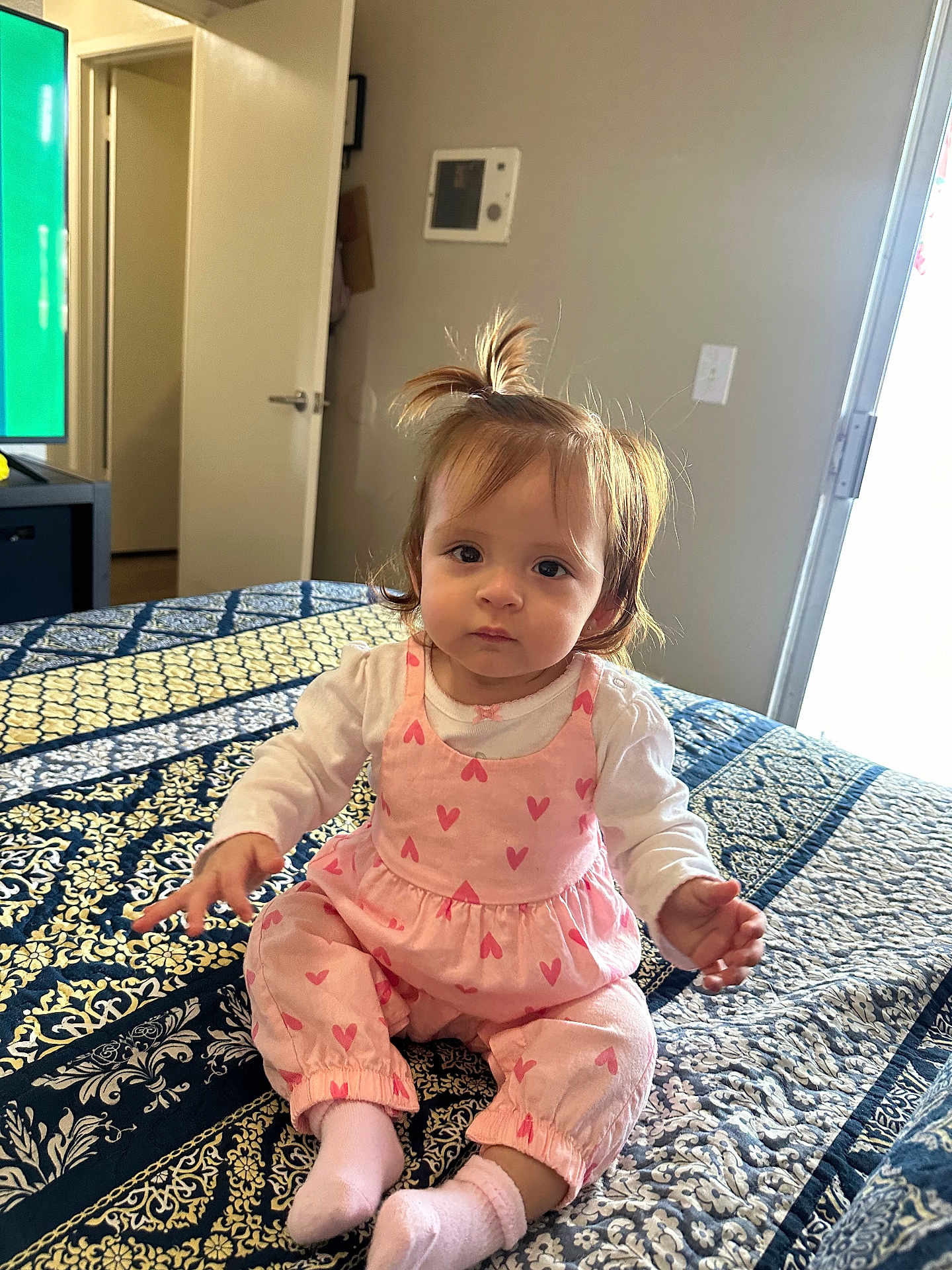 Ivanna is registered to the contest to win money with this photo: toddler, child, baby, indoor, bed, blanket, pink_clothing, heart_pattern, socks, person, face, hair, curious, sitting, room, door, light, window, comfort, portrait
