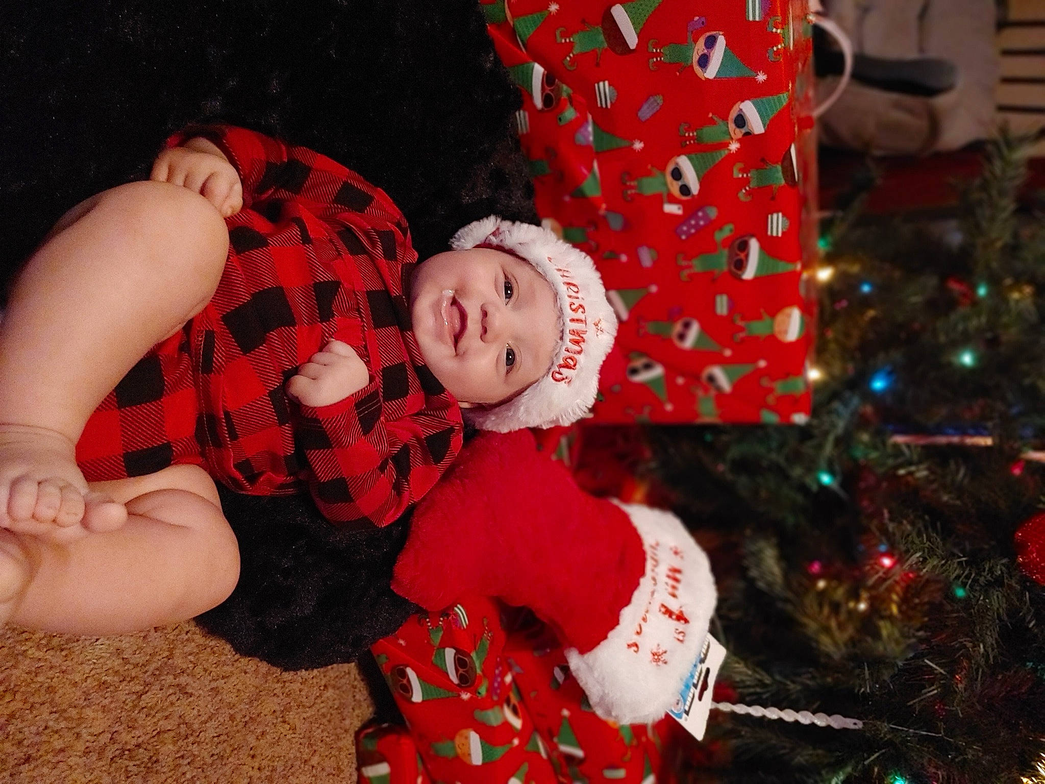 Jazlyn is registered to the contest to win money with this photo: baby, baby_toddler_clothing, beauty, child, christmas, christmas_decoration, christmas_tree, event, facial_expression, fun, happy, head, headwear, holiday, joy, lap, person, plant, red, sock