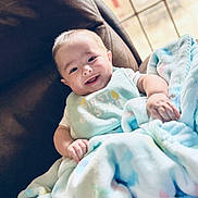 Alonso is registered to the contest to win money with this photo: baby, smiling, blanket, chair, indoors, window, happy, cozy, comfort, infant, child, soft, pastel, clothing, home, portrait, cute, relaxed, person, natural_light