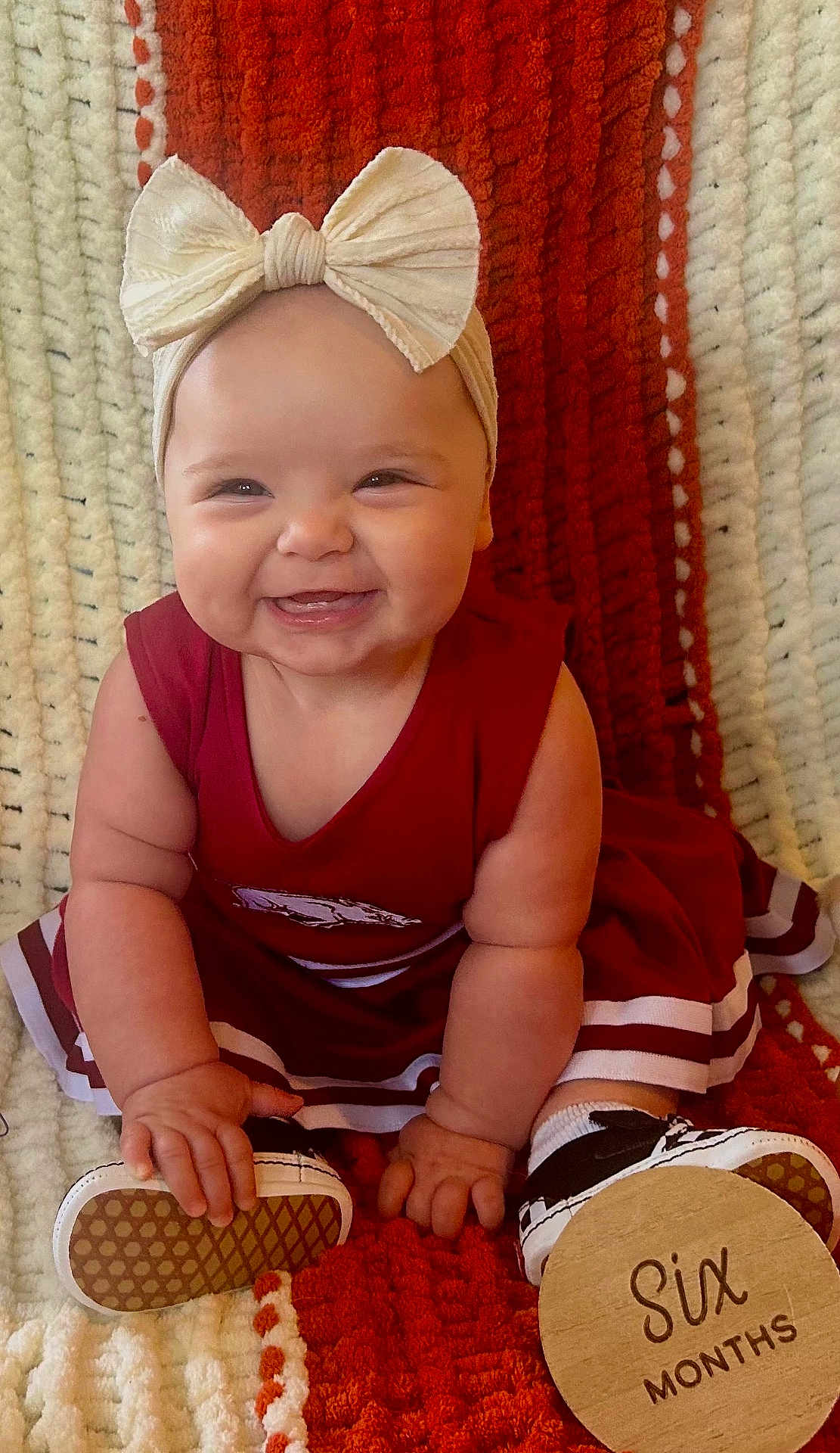 Aubrey is registered to the contest to win money with this photo: baby, infant, smiling, red_dress, headband, bow, shoe, plaque, six_months, milestone, blanket, texture, cute, happy, chubby_cheeks, sitting, hands, feet, indoors, portrait