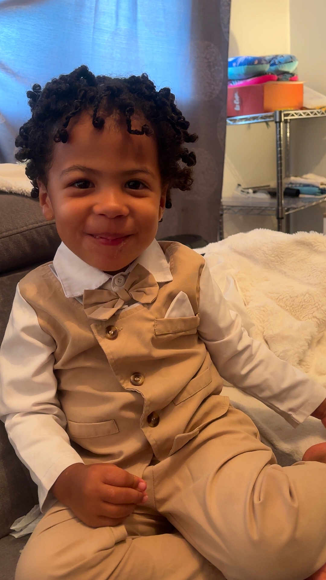 Laurentiu participe au concours pour gagner de l'argent avec cette photo : child, smile, curly_hair, beige_vest, bow_tie, white_shirt, sitting, indoor, couch, blanket, hand, portrait, happy, home, cute, toddler, face, furniture, window, curtain