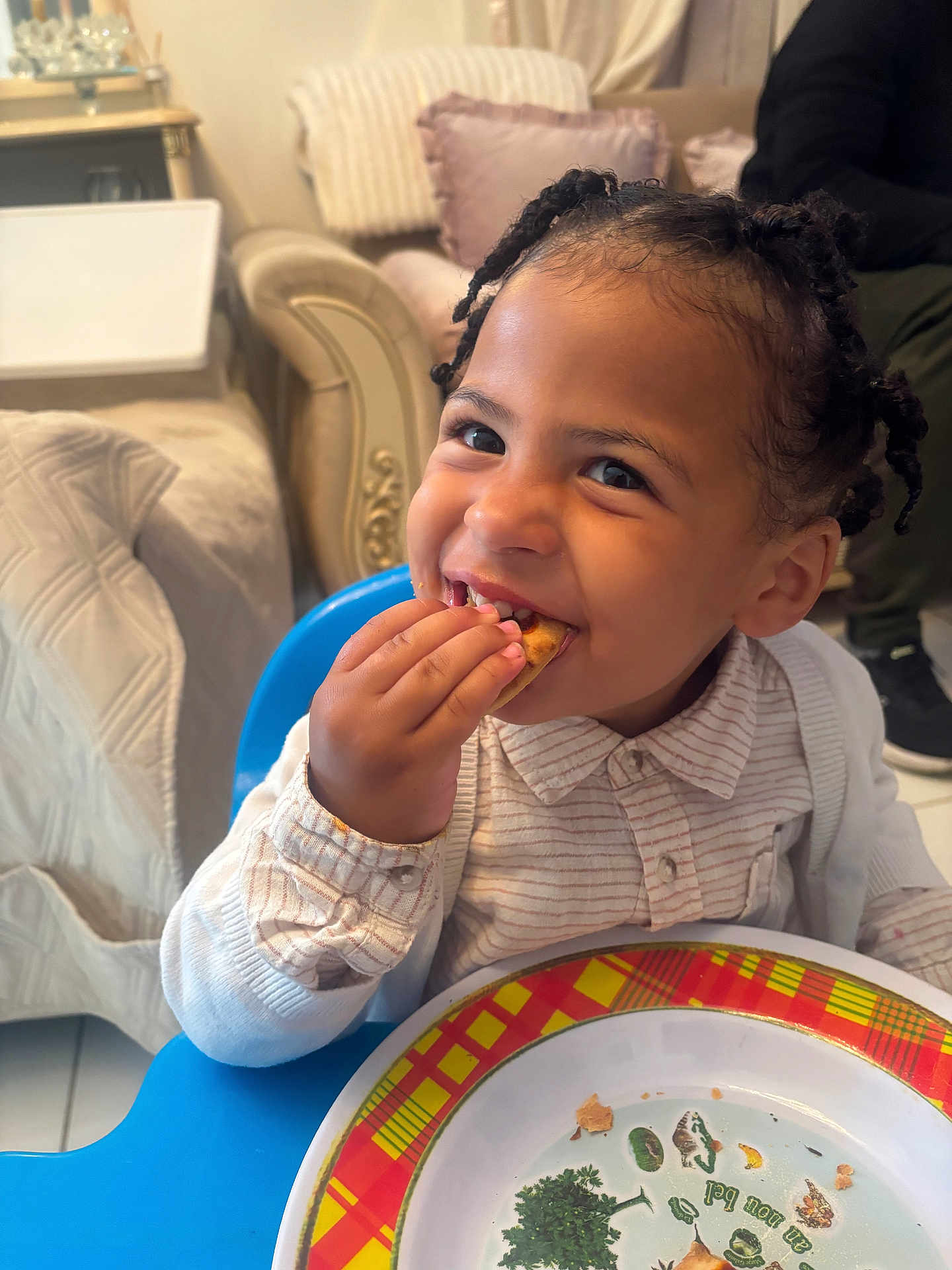 Laurentiu a rejoint le concours — aidez-le/la à gagner de superbes lots ! child, toddler, smile, eating, plate, food, high_chair, braided_hair, indoor, furniture, couch, pillow, person, clothing, tableware, happy, face, hand, home, snack