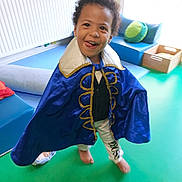 Laurentiu participe au concours pour gagner de l'argent avec cette photo : toddler, child, cape, blue_cape, barefoot, playful, smiling, indoor, green_mat, cushions, toys, radiator, wooden_box, curly_hair, happy, person, young_child, floor, room, casual_clothing