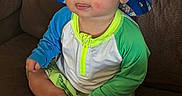 Jackson joined the competition — help win amazing prizes! baby, child, hat, bucket_hat, fish_pattern, tongue_out, sitting, couch, brown_couch, colorful_clothing, long_sleeve_shirt, green_sleeves, shorts, barefoot, hand, indoor, cute, playful, face, person