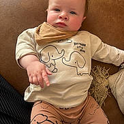 Munro joined the competition — help win amazing prizes! baby, child, infant, pointing, brown_couch, elephant_print, beige_shirt, pants, scarf, indoor, cute, face, person, young_child, sitting, clothing, skin, hand, expression, furniture