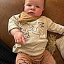 baby, child, infant, pointing, brown_couch, elephant_print, beige_shirt, pants, scarf, indoor, cute, face, person, young_child, sitting, clothing, skin, hand, expression, furniture
