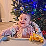 Juniper joined the competition — help win amazing prizes! baby, child, high_chair, plush_toy, christmas_tree, ornaments, lights, holiday, indoor, smiling, pajamas, infant, festive, decoration, happy, cute, face, person, celebration, home