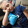 blue_shirt, boy, car, casual_clothing, child, closed_eyes, daylight, denim_shorts, indoors, peaceful, pillow, portrait, relaxed, resting, seat, seatbelt, sleeping, travel, window, young