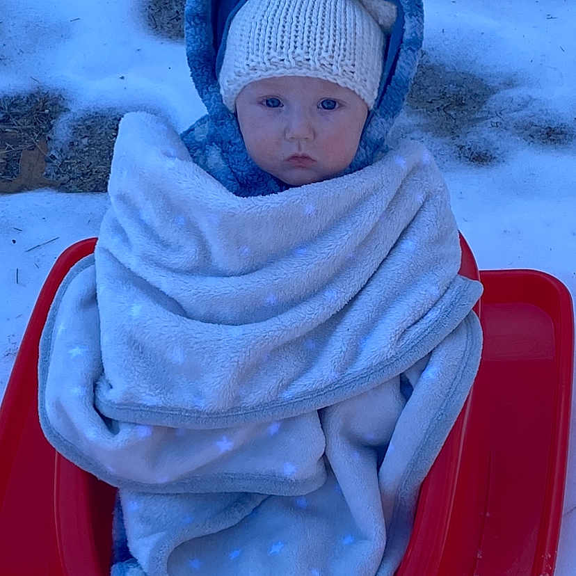 Julian is registered to the contest to win money with this photo: baby, beanie, blanket, bonnet, cap, clothing, face, glove, happy, hat, head, hood, ice, person, photography, portrait, sled, slide, smile, winter