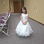 child, girl, white_dress, indoor, carpet, folding_chairs, closed_door, exit_sign, wall, smile, long_hair, young, person, event, formal, standing, room, furniture, happy, portrait