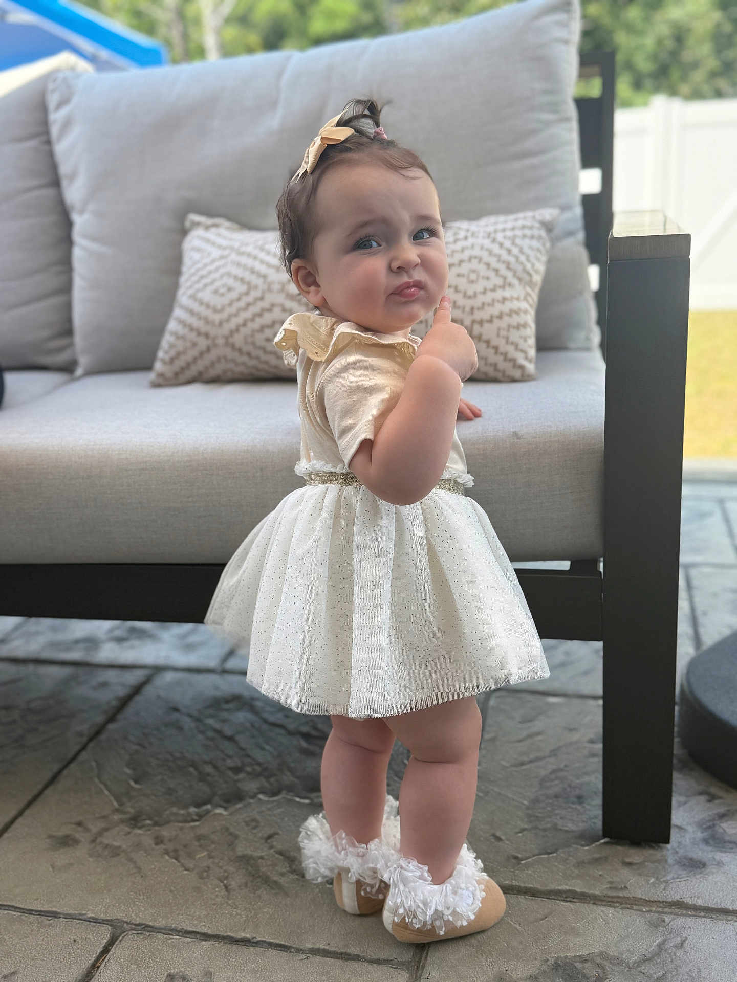 Elissa joined the competition — help win amazing prizes! toddler, child, dress, white_dress, baby, shoes, frilly_shoes, outdoor, patio, stone_floor, sofa, cushion, curious_expression, pointing, hair_bow, person, standing, cute, young_child, fashion