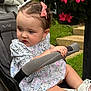 toddler, child, stroller, flower, pink_bow, white_bow, floral_dress, lace_socks, pink_shoes, grass, garden, greenery, hand, face, hair, outdoor, seat, person, infant, cute