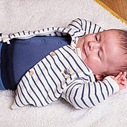 Timéo participe au concours pour gagner de l'argent avec cette photo : baby, infant, blanket, striped_clothing, blue_pants, teddy_bear_emblem, soft_texture, lying_down, relaxed, peaceful, child, portrait, indoor, cute, small_hands, head, face, sleepy, warm_clothing, wooden_floor