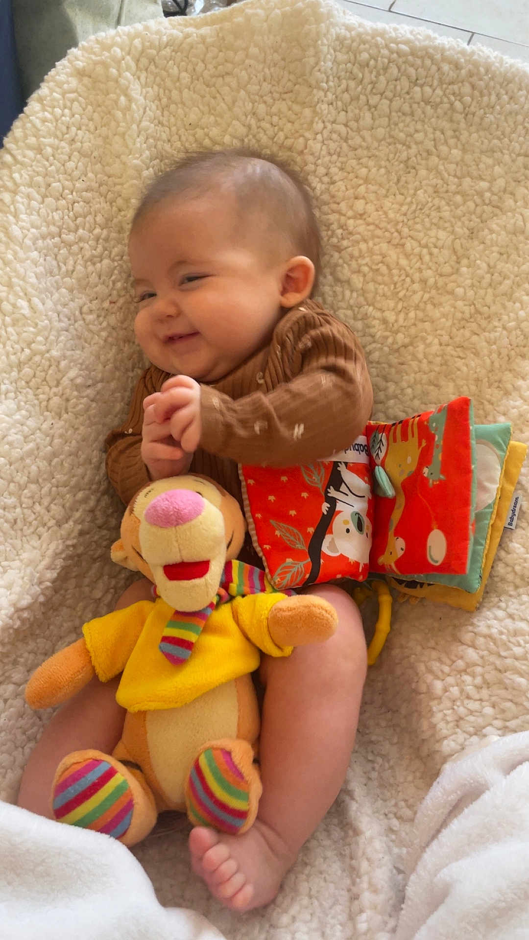 Lily-Honora participe au concours pour gagner de l'argent avec cette photo : baby, smiling, toy, stuffed_animal, fabric_book, blanket, cozy, infant, cute, happy, child, colorful, soft, playtime, indoors, foot, clothing, person, portrait, relaxing