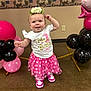 baby, balloons, birthday, celebration, child, decor, face, first_birthday, floor, flower_crown, indoor, pink, polka_dot, shirt, skirt, smiling, sneakers, standing, wall, white