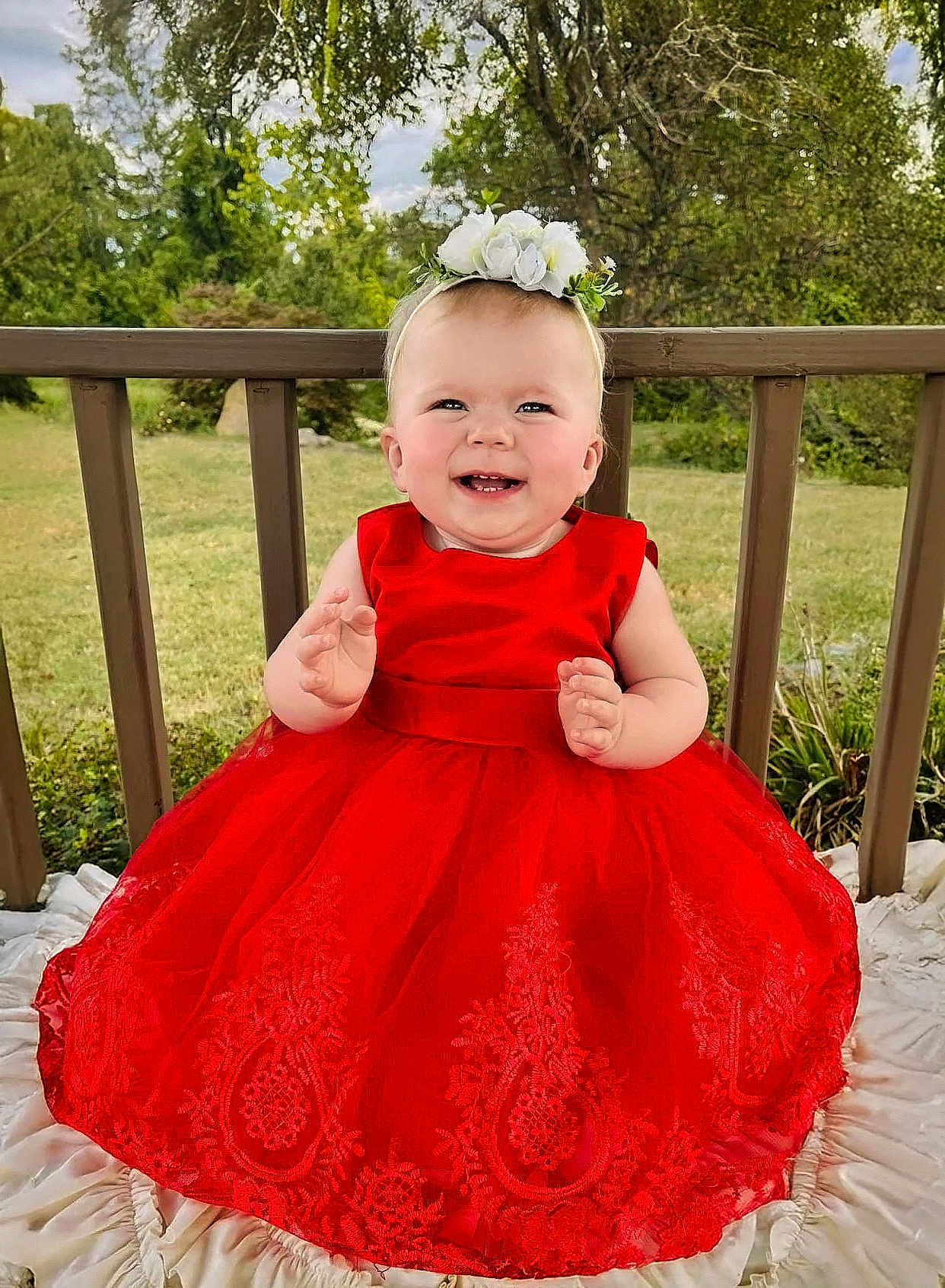 Adalynn joined the competition — help win amazing prizes! baby, child, red_dress, flower_headband, smiling, outdoor, grass, wooden_railing, blanket, portrait, happy, nature, greenery, infant, cute, sitting, headband, dress, young_child, sunlight