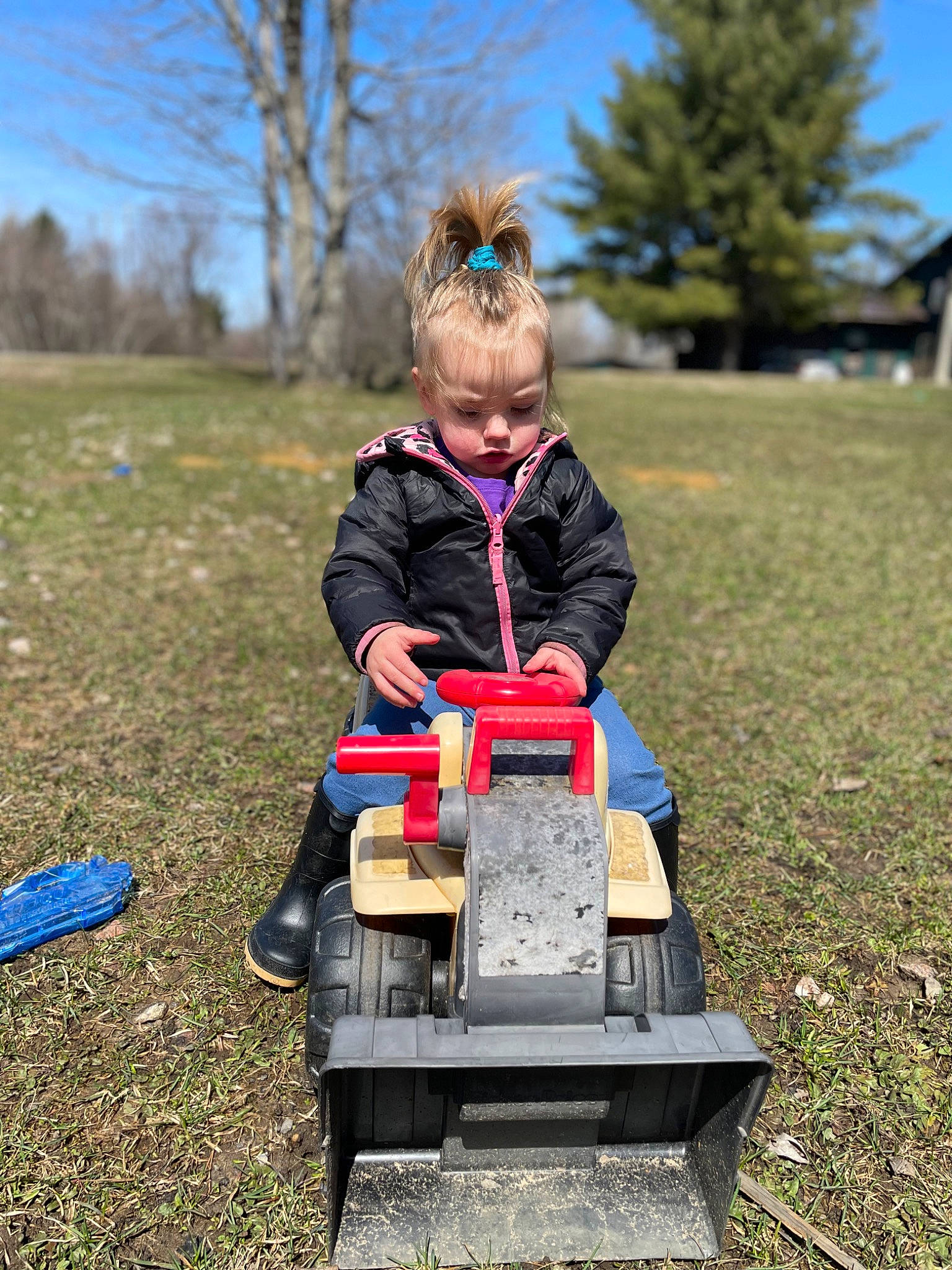 Amyah is registered to the contest to win money with this photo: field, fun, grass, grassland, jacket, leisure, motor_vehicle, people_in_nature, person, plant, recreation, rolling, rural_area, sitting, sky, soil, tire, toddler, tree, vehicle