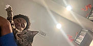 Billie is registered to the contest to win money with this photo: cat, person, indoor, ceiling, light, lamp, tabby_cat, whiskers, paw, curious, holding, face, afro_hair, blue_shirt, vent, feline, pet, close_up, human, room