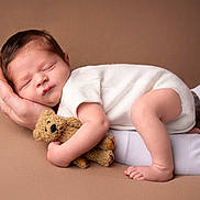 Léo participe au concours pour gagner de l'argent avec cette photo : baby, newborn, sleeping_baby, teddy_bear, hand, parent_hand, white_clothing, brown_background, portrait, studio, soft_texture, cozy, infant, cute, peaceful, bare_foot, toes, face, head, plush_toy