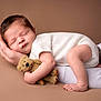baby, newborn, sleeping_baby, teddy_bear, hand, parent_hand, white_clothing, brown_background, portrait, studio, soft_texture, cozy, infant, cute, peaceful, bare_foot, toes, face, head, plush_toy