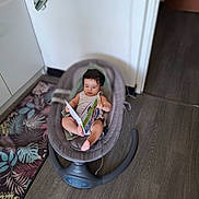 Daniel a rejoint le concours — aidez-le/la à gagner de superbes lots ! baby, child, reading, book, baby_rocker, floor, rug, indoor, home, footwear, slipper, wooden_floor, person, clothing, seat, furniture, face, hair, expression, relaxation