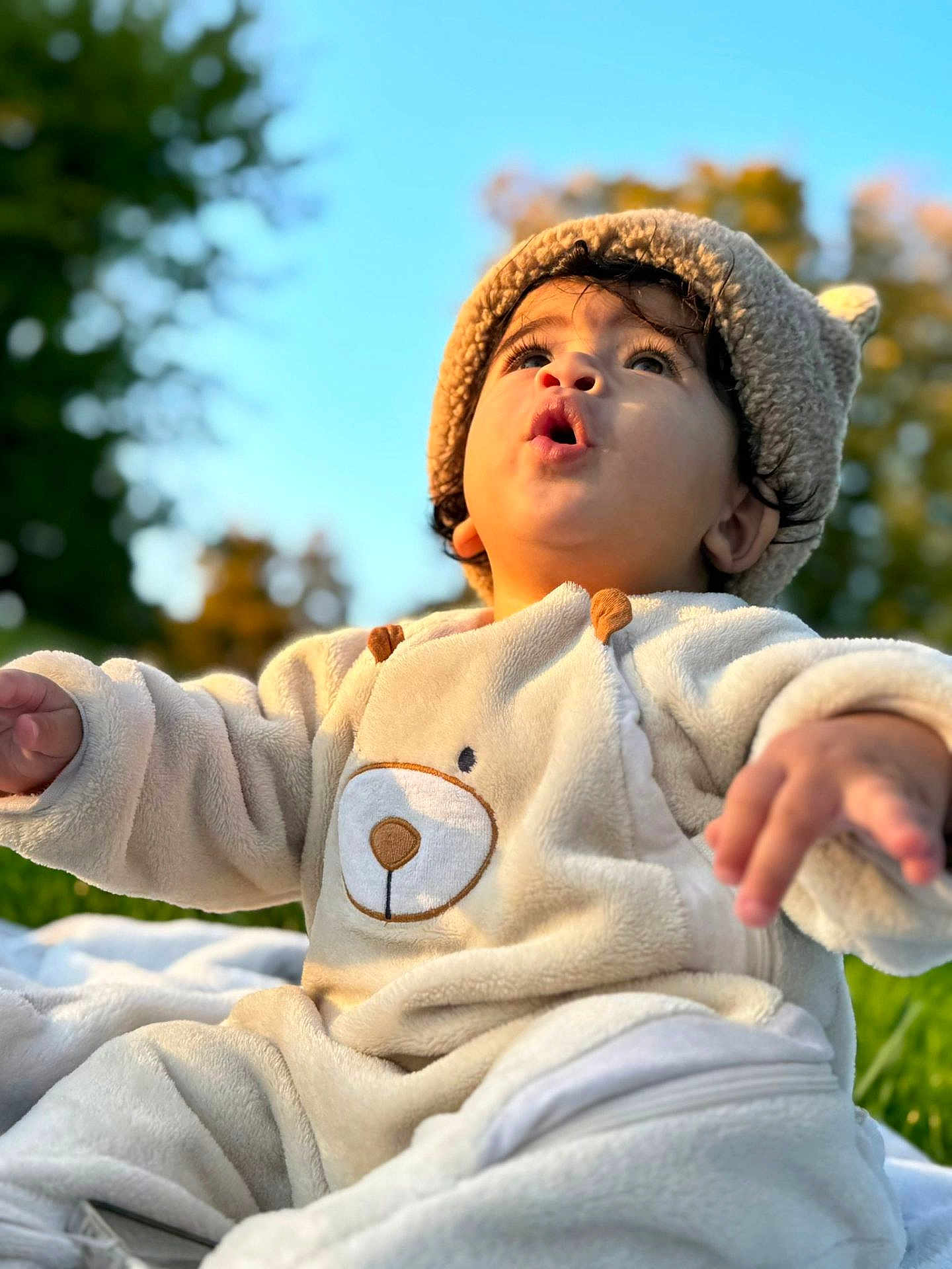Daniel participe au concours pour gagner de l'argent avec cette photo : baby, child, outdoor, blue_sky, greenery, cute, cozy_clothing, bear_outfit, hat, curious, expression, portrait, soft_texture, warm_lighting, sitting, nature, infant, adorable, face, daylight