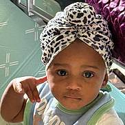 Sianni is registered to the contest to win money with this photo: baby, infant, child, portrait, face, eyes, serious_expression, headwrap, leopard_print, bow, bib, shirt, sitting, indoor, bedroom, furniture, quilt, sunlight, close_up, photography