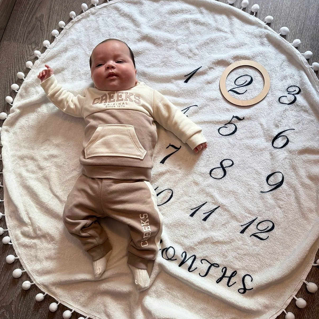 Jules a rejoint le concours — aidez-le/la à gagner de superbes lots ! age_marker, baby, blanket, child, clothing, cozy, cute, face, flooring, indoor, infant, lying_down, months, numbers, person, portrait, round_blanket, socks, wood_floor, wooden_ring