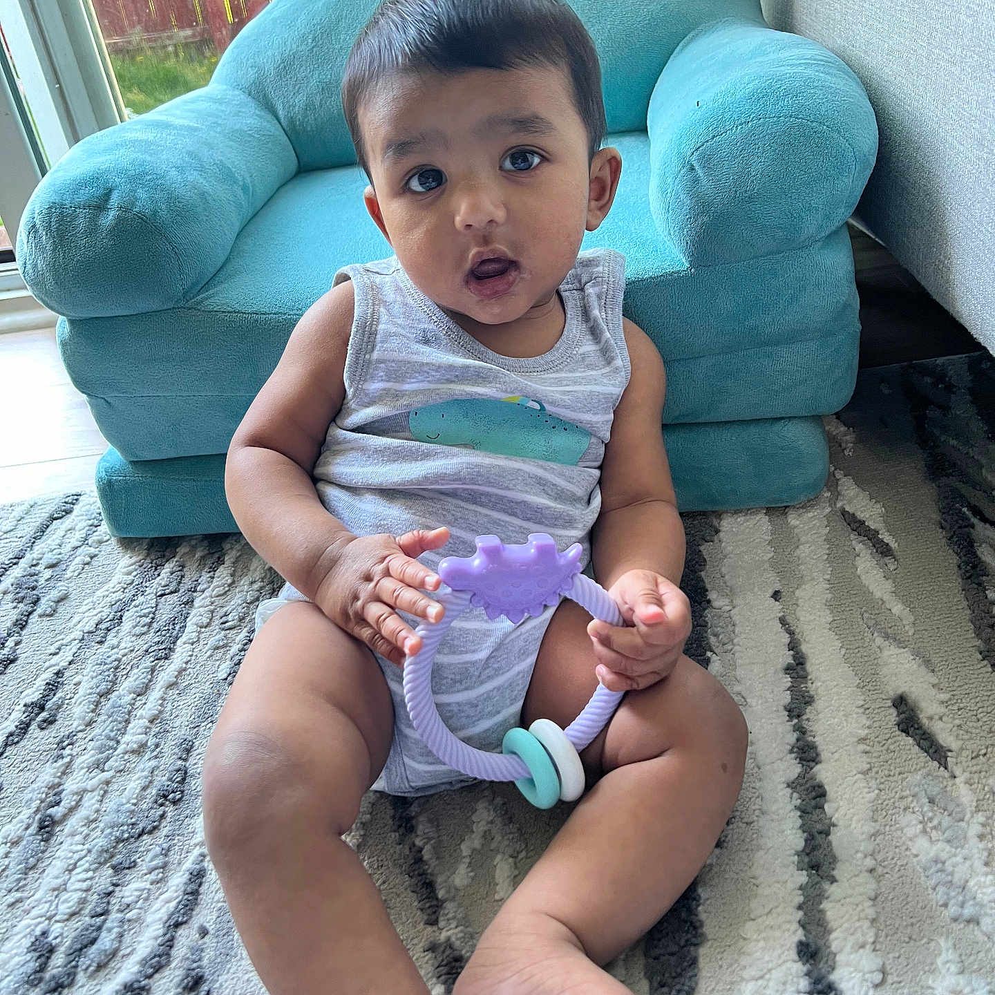 Aman Kobir is registered to the contest to win money with this photo: armchair, baby, carpet, casual_clothing, child, curious, cute, expression, floor, home, indoor, infant, natural_light, playtime, plush_furniture, sitting, soft_skin, teething_ring, toy, window