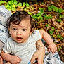 baby, child, infant, person, arm, hand, tattoo, nails, blue_nail_polish, curly_hair, gray_shirt, outdoor, nature, leaves, greenery, looking_up, expression, skin, holding, adult