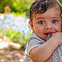 baby, child, blue_eyes, cute, close_up, outdoor, nature, person, portrait, hand, chewing, clothing, adult_arm, soft_light, curly_hair, skin, fabric, expression, holding, daylight