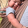 baby, infant, child, face, skin, hand, arm, baby_carrier, fabric, outdoor, sunlight, person, close_up, happy, smile, holding, casual_clothing, texture, parent, affection