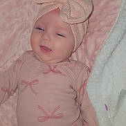 Kezmai is registered to the contest to win money with this photo: baby, infant, pink_clothing, headband, bow, blanket, soft_texture, smiling, lying_down, cute, child, indoors, cozy, apparel, face, person, newborn, sleepy, happy, comfort