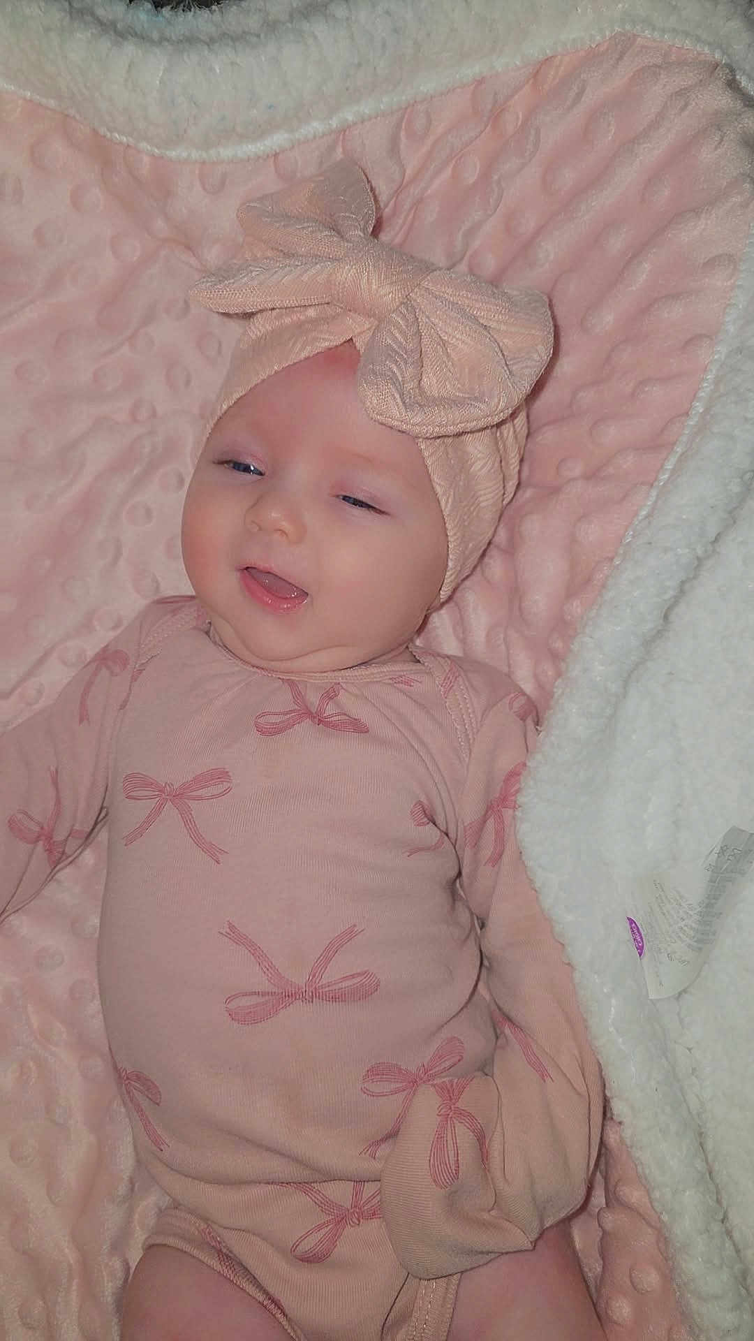 Kezmai is registered to the contest to win money with this photo: baby, infant, pink_clothing, headband, bow, blanket, soft_texture, smiling, lying_down, cute, child, indoors, cozy, apparel, face, person, newborn, sleepy, happy, comfort