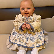 Asaël participe au concours pour gagner de l'argent avec cette photo : baby, child, smile, dress, floral_pattern, sitting, couch, cushion, happy, cute, portrait, indoors, sock, hands, head, face, person, clothing, furniture, infant
