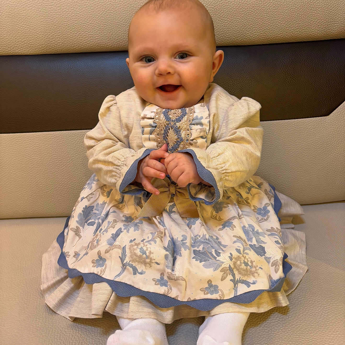 Asaël participe au concours pour gagner de l'argent avec cette photo : baby, child, clothing, couch, cushion, cute, dress, face, floral_pattern, furniture, hands, happy, head, indoors, infant, person, portrait, sitting, smile, sock