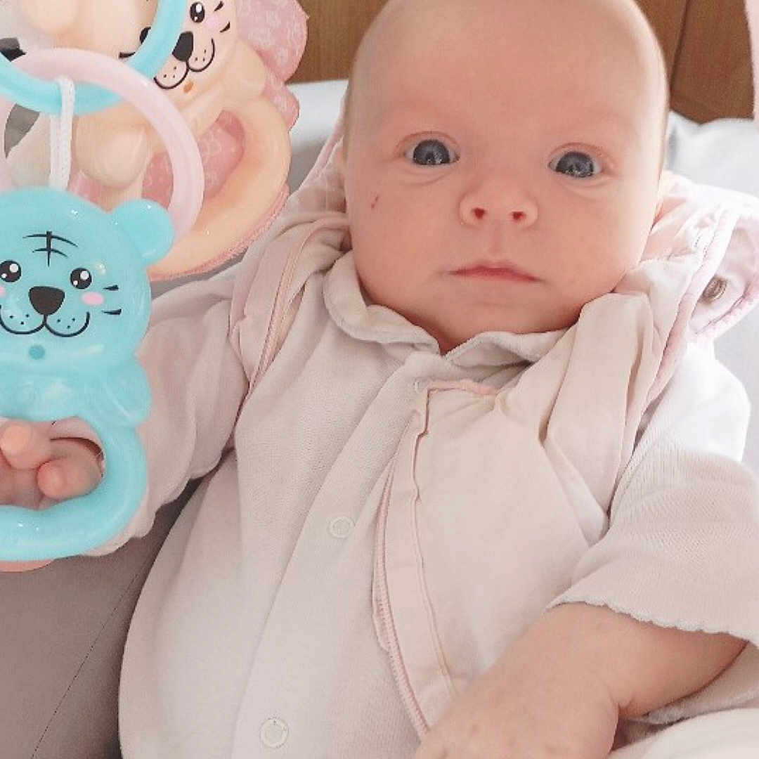 Marie Line Maiia participe au concours pour gagner de l'argent avec cette photo : baby, infant, toy, plastic_toy, blue_toy, pink_toy, hand, face, eyes, blanket, clothing, onesie, indoor, wooden_background, cute, child, person, portrait, soft_light, baby_girl