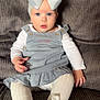 baby, child, blue_eyes, white_bow, dress, tights, sitting, couch, gray_couch, plush, long_sleeve_shirt, indoor, cute, portrait, infant, fashion, clothing, person, young_child, headwear