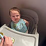 baby, high_chair, food, bib, green_food, hand, feeding, expression, face, messy, indoor, child, person, meal, tray, clothing, cute, funny, tongue, dining
