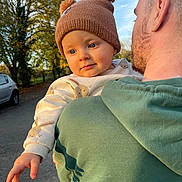 Marcel participe au concours pour gagner de l'argent avec cette photo : baby, child, person, adult, hat, pom_pom, sweater, bunny_pattern, outdoor, trees, car, autumn, sunlight, green_hoodie, face, hand, road, portrait, warm_light, casual_clothing