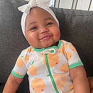 Savani Sage is registered to the contest to win money with this photo: baby, child, smiling, headband, bow, onesie, orange_pattern, couch, indoor, face, cute, cheeks, infant, sitting, happy, person, clothing, textile, portrait, home