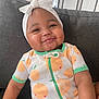 baby, child, smiling, headband, bow, onesie, orange_pattern, couch, indoor, face, cute, cheeks, infant, sitting, happy, person, clothing, textile, portrait, home