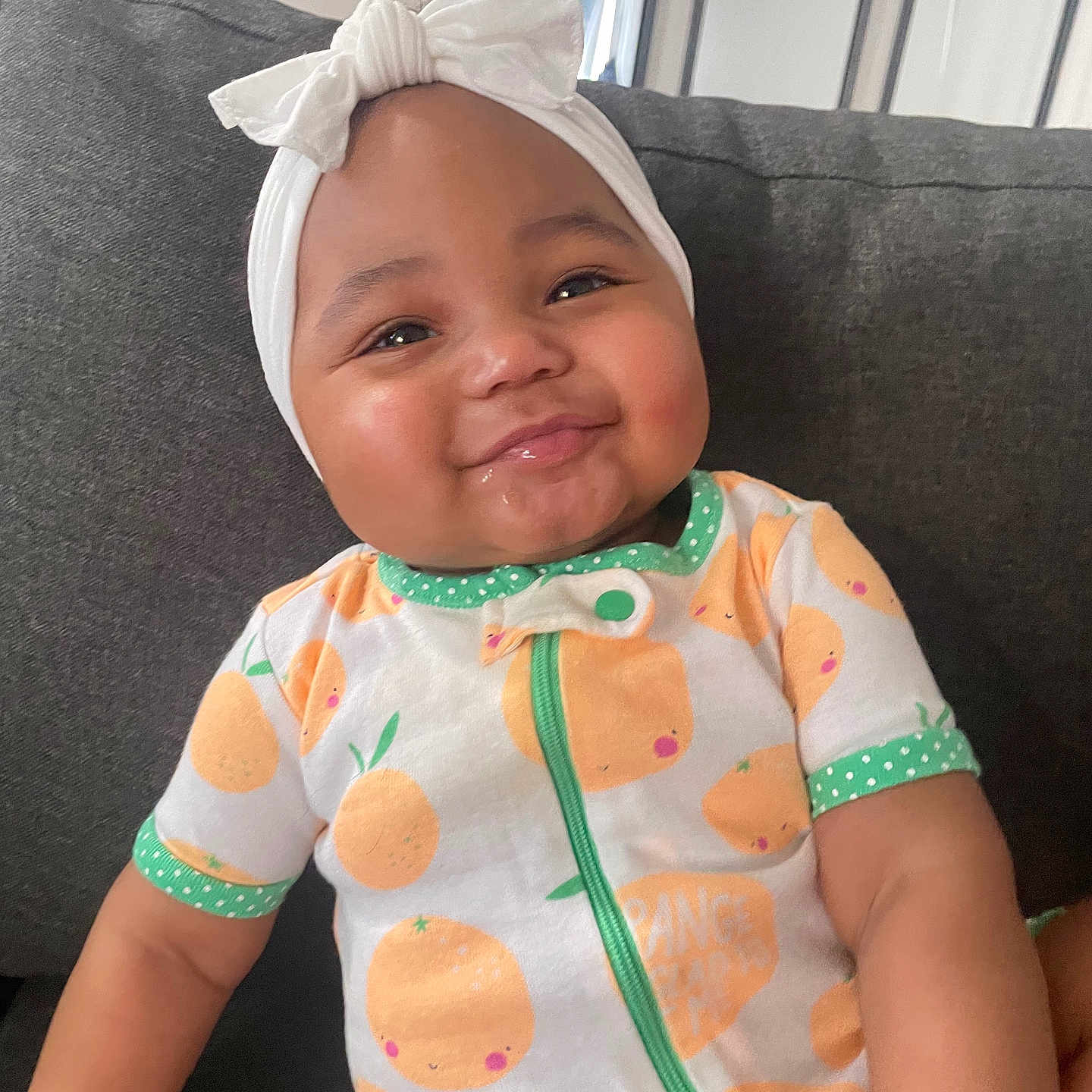 Savani Sage is registered to the contest to win money with this photo: baby, bow, cheeks, child, clothing, couch, cute, face, happy, headband, home, indoor, infant, onesie, orange_pattern, person, portrait, sitting, smiling, textile