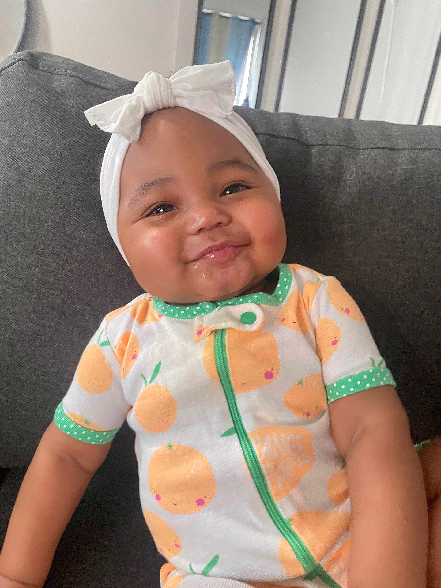 Savani Sage is registered to the contest to win money with this photo: baby, child, smiling, headband, bow, onesie, orange_pattern, couch, indoor, face, cute, cheeks, infant, sitting, happy, person, clothing, textile, portrait, home