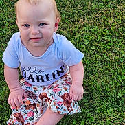 Rowyn is registered to the contest to win money with this photo: baby, child, grass, outdoor, sitting, shirt, skirt, dog_print, crossed_legs, barefoot, cute, young_child, nature, portrait, daylight, blue_eyes, short_hair, expression, clothing, person
