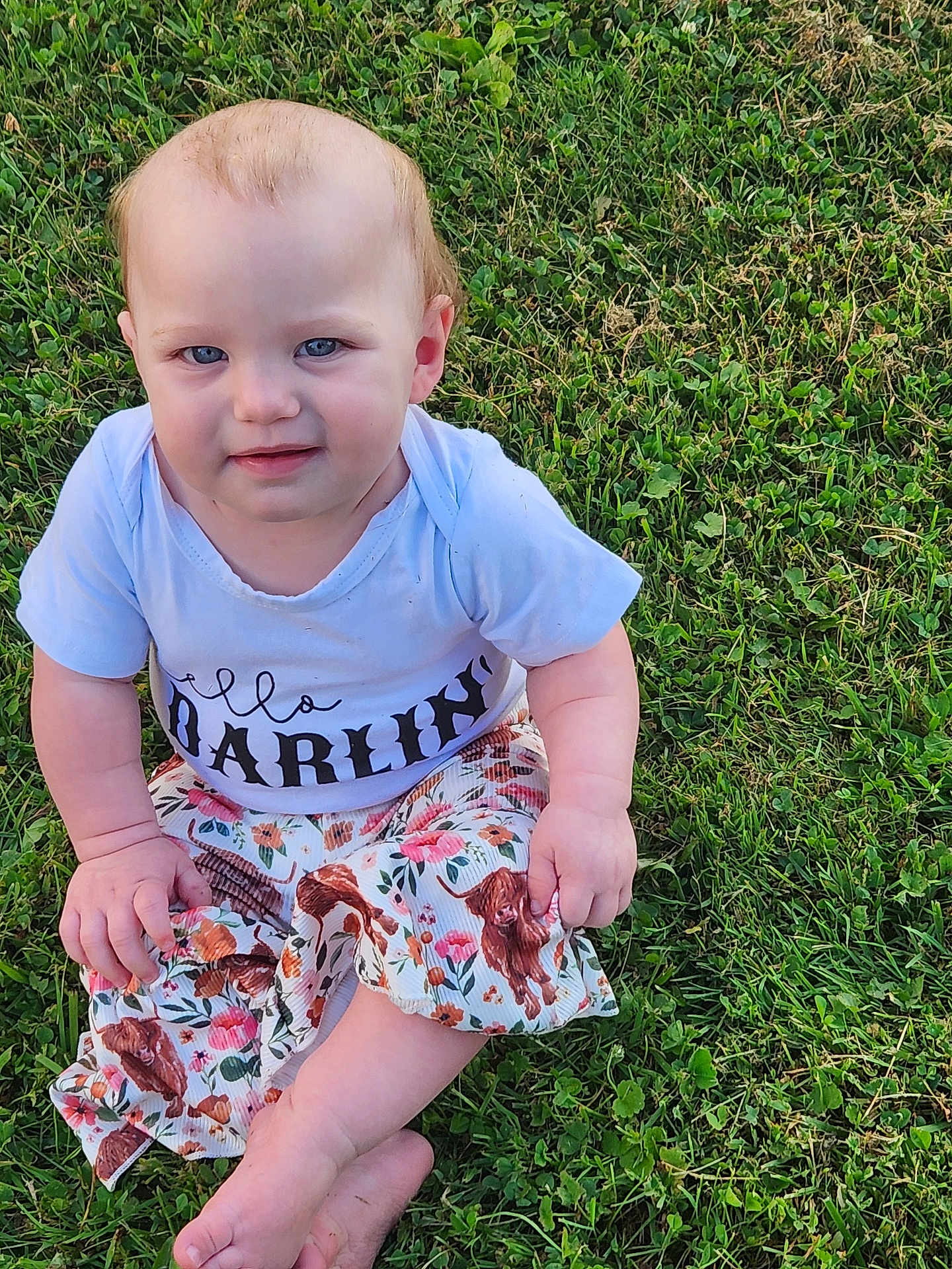 Rowyn is registered to the contest to win money with this photo: baby, child, grass, outdoor, sitting, shirt, skirt, dog_print, crossed_legs, barefoot, cute, young_child, nature, portrait, daylight, blue_eyes, short_hair, expression, clothing, person