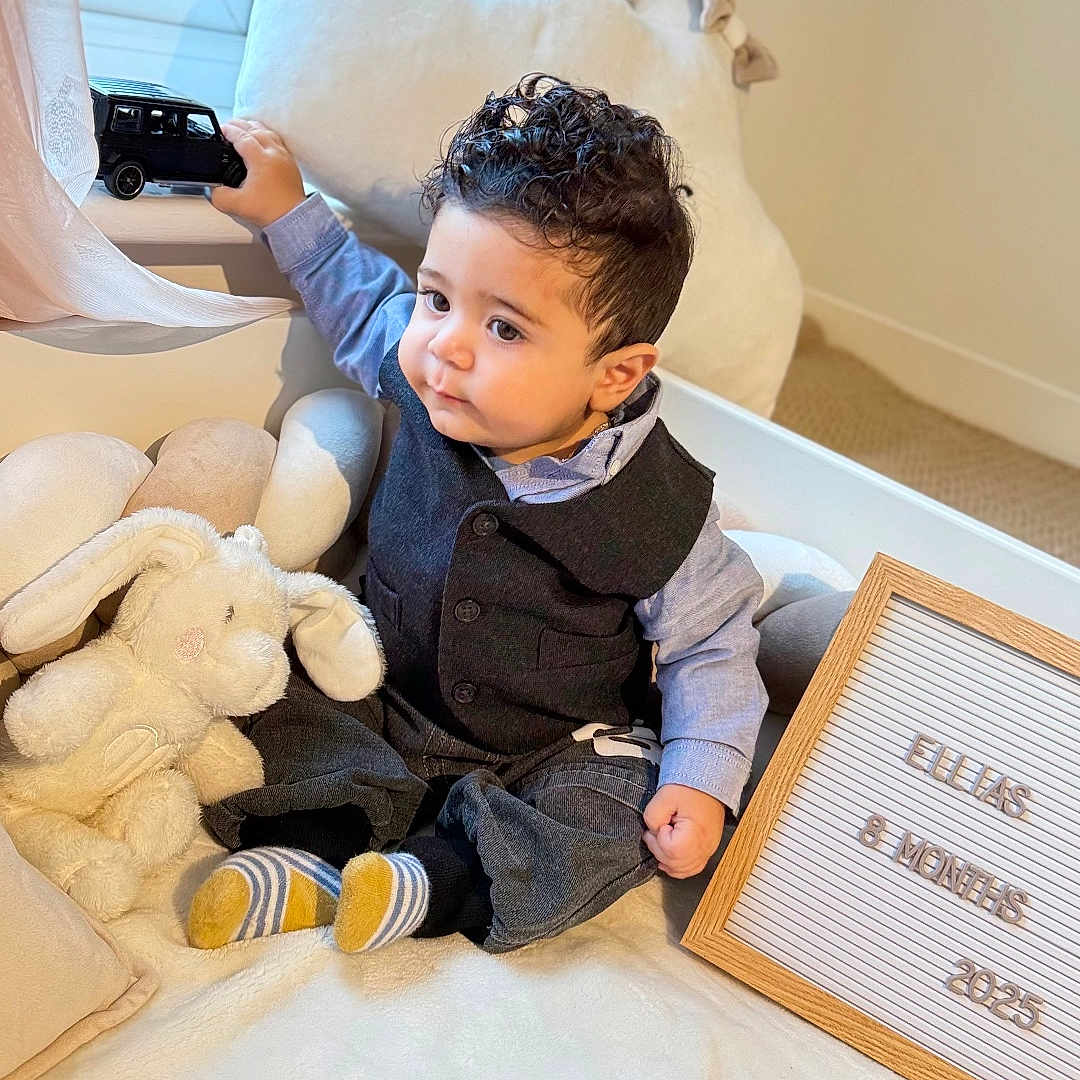 Ellias joined the competition — help win amazing prizes! baby, bed, car_toy, child, clothing, cute, indoor, infant, letter_board, milestone, natural_light, plush_toy, portrait, smiling, socks, soft_fabric, stuffed_animal, toy, vest, window