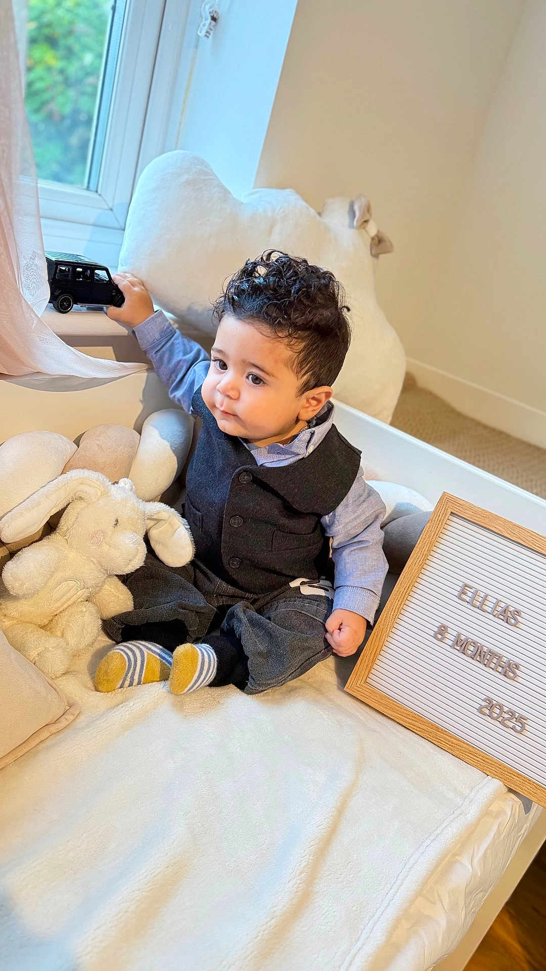 Ellias joined the competition — help win amazing prizes! baby, bed, car_toy, child, clothing, cute, indoor, infant, letter_board, milestone, natural_light, plush_toy, portrait, smiling, socks, soft_fabric, stuffed_animal, toy, vest, window