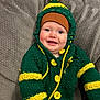 baby, infant, child, smile, happy, knit_hat, pom_pom, sweater, cardigan, green_sweater, yellow_buttons, cozy, blanket, couch, portrait, rosy_cheeks, blue_eyes, sitting, adorable, closeup